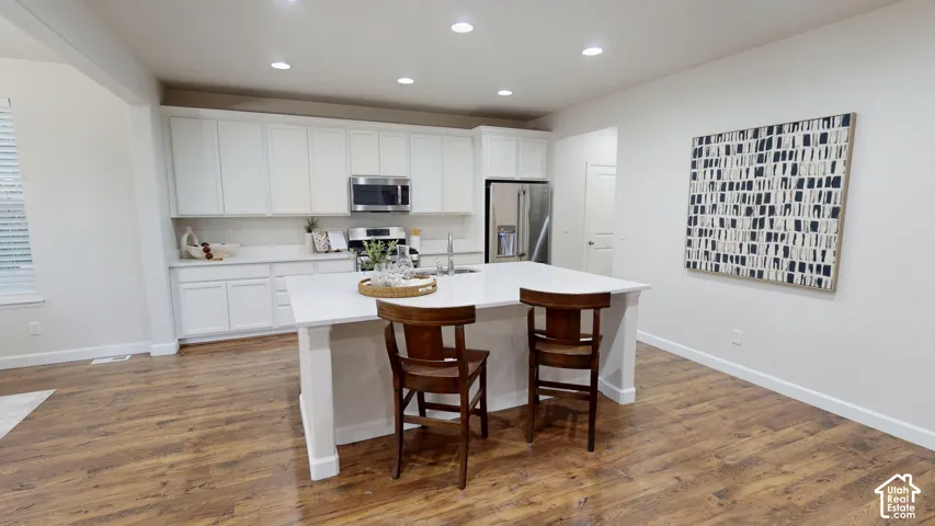Kitchen featuring white cabinetry, center island with stone-finish countertop, stainless steel appliances, recessed lighting, and wood-finish flooring