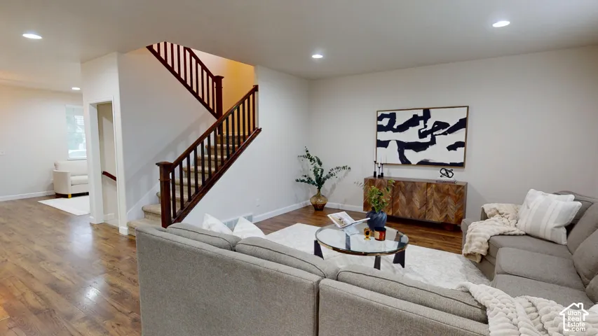 Open-concept interior featuring wood-finish flooring, recessed lighting, and a prominent staircase with dark-stained wood railings