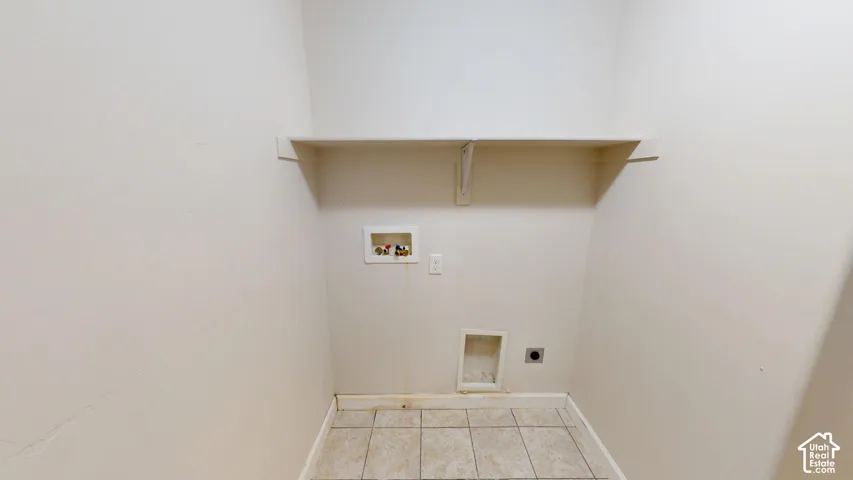 Utility area featuring tile flooring, a wall-mounted storage shelf, and dedicated water, electrical, and ventilation hookups