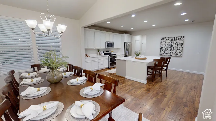 Open-concept kitchen and dining area featuring white shaker-style cabinetry, a central island with quartz countertops, stainless steel appliances, recessed lighting, and wood-finish flooring