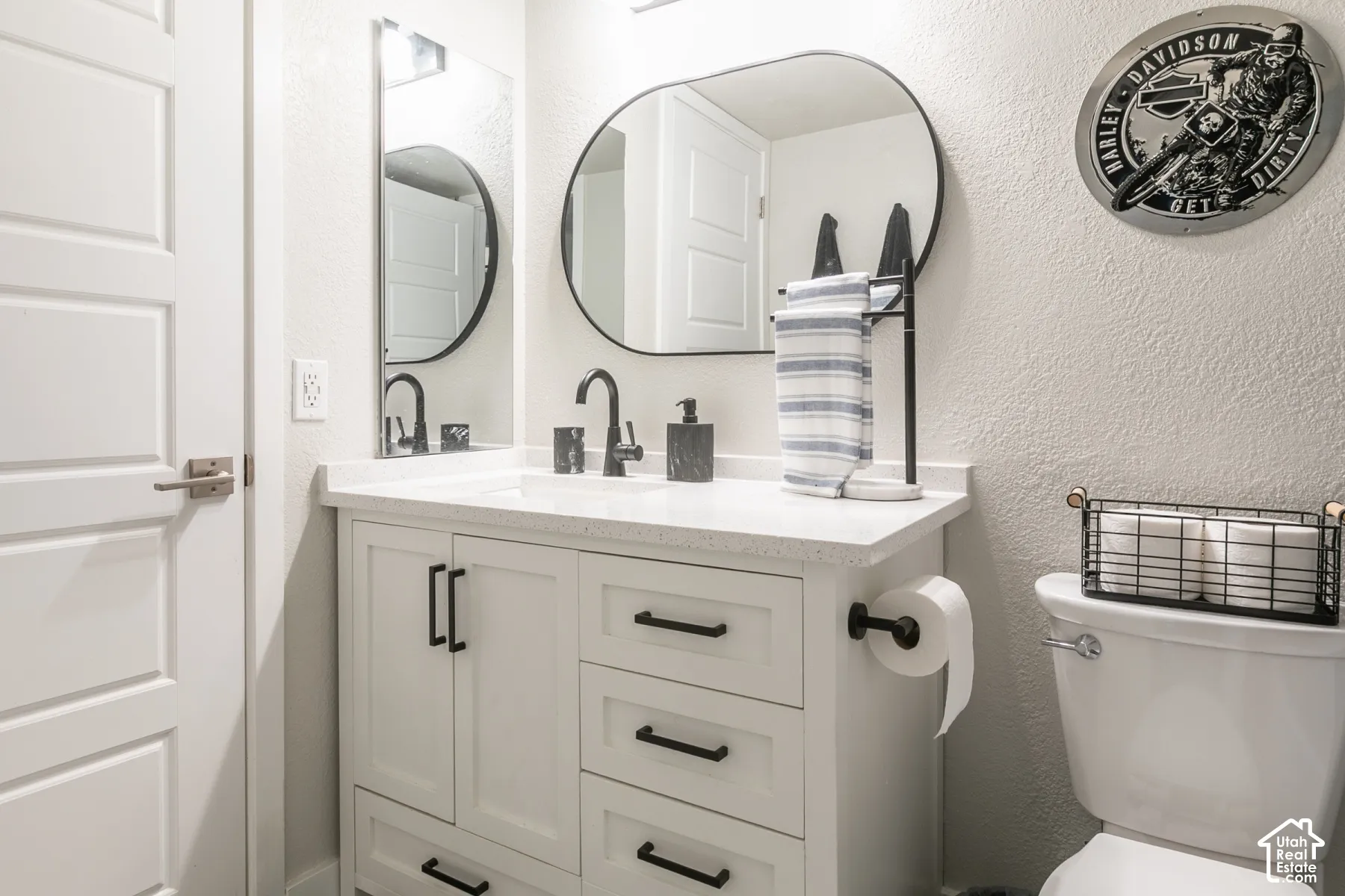 Bathroom vanity with white cabinetry, light-toned composite countertop, oval mirror, and matte black hardware