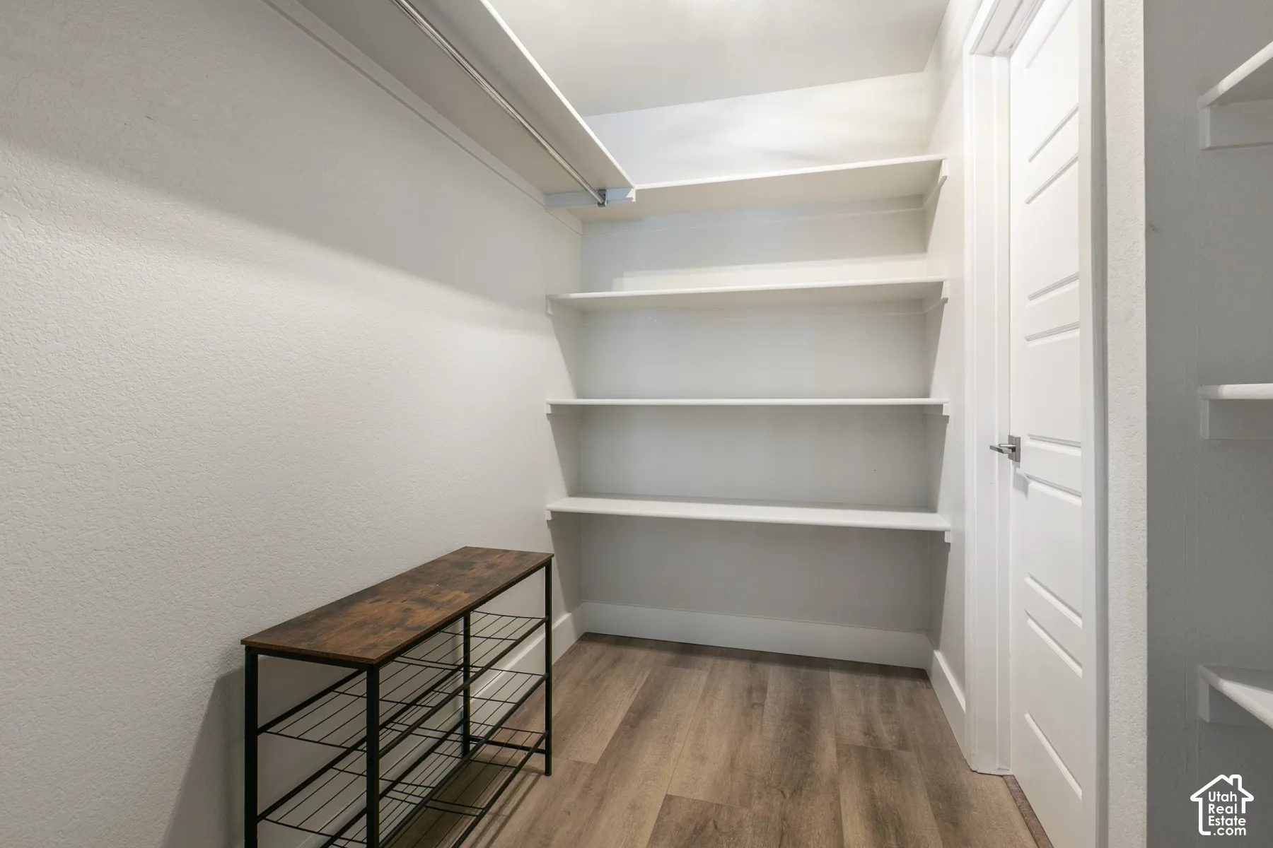 Walk-in closet featuring wood-finish flooring, built-in shelving, a metal hanging rod, and a multi-panel door