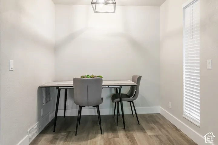 Neutral interior space featuring wood-finish flooring, a contemporary geometric pendant light fixture, and horizontal window blinds