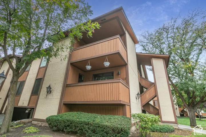 Multi-story exterior featuring textured stucco siding, vertical wood paneling, stacked private balconies, and integrated outdoor lighting fixtures
