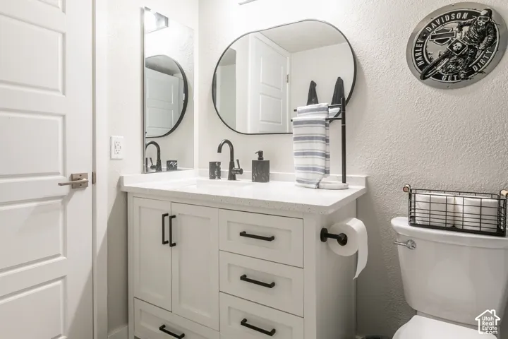 Bathroom vanity with white cabinetry, light-toned composite countertop, oval mirror, and matte black hardware