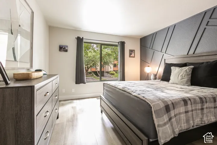 Bedroom featuring a dark-toned geometric accent wall, wood-finish flooring, and a large sliding window