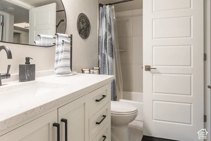Bathroom featuring a vanity with a light-toned countertop, integrated rectangular sink, matte black hardware, a circular wall-mounted mirror, and a tub-shower combination with light-toned wall tile