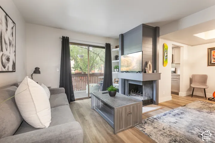 Living area featuring wood-finish flooring, a floor-to-ceiling fireplace with horizontal shiplap detailing, built-in shelving, and sliding glass doors