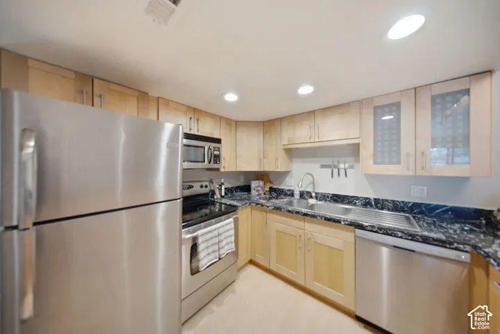 Kitchen featuring light wood cabinetry, stainless steel appliances, dark granite countertops, an undermount sink, and recessed lighting
