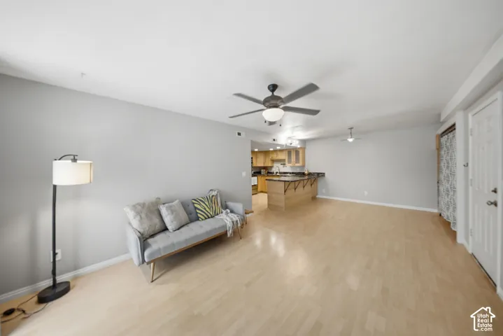 Open-concept living area with light wood-finish flooring, light gray wall paint, and a ceiling fan with integrated lighting