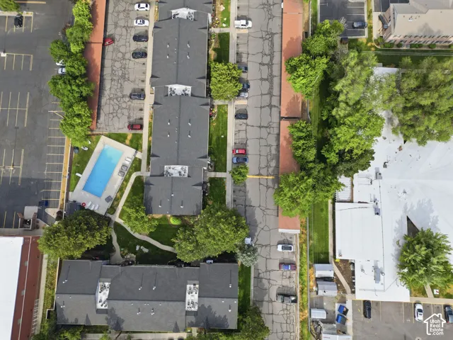 Aerial perspective showcasing multiple residential buildings with dark-shingled roofs, surrounding a rectangular swimming pool with an adjacent paved patio