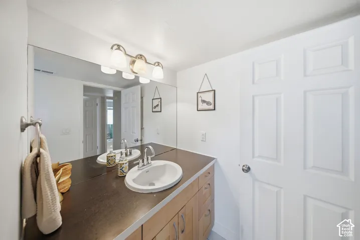 Bathroom vanity featuring a light wood-finish base, dark countertop, and dual sinks with chrome faucets