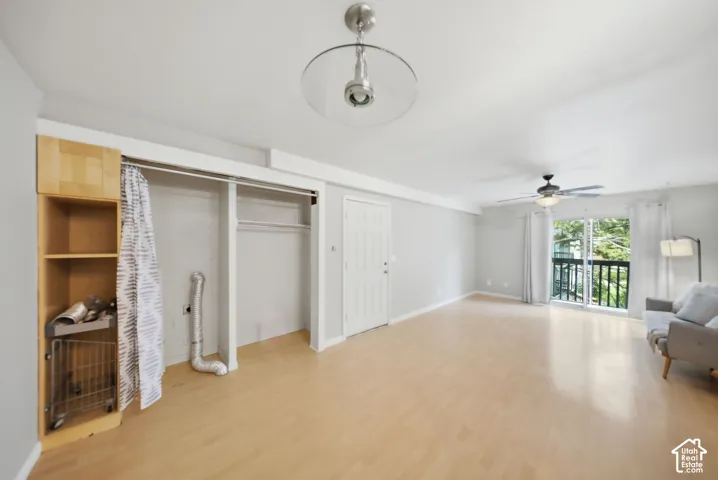 Spacious room with wood-finish flooring, a ceiling fan with integrated lighting, and a sliding glass door opening to a balcony