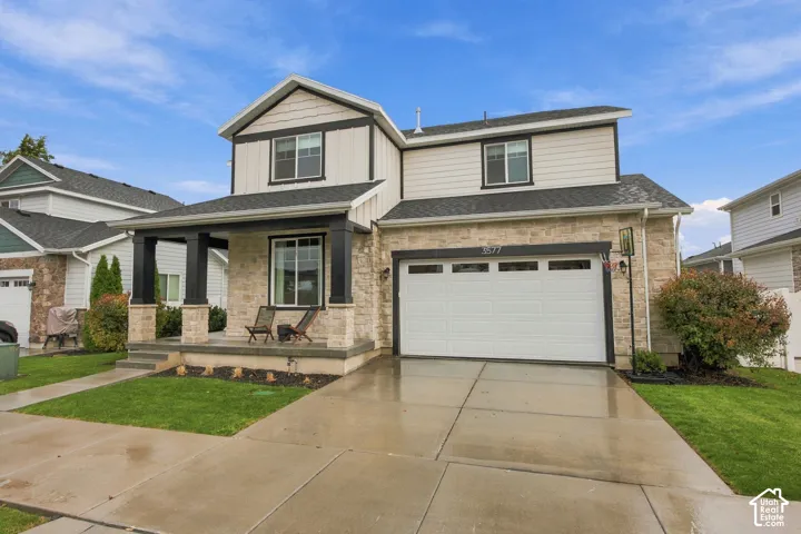 Two-story exterior featuring stone veneer siding, vertical and horizontal board finishes, a covered front porch with prominent columns, and an attached two-car garage