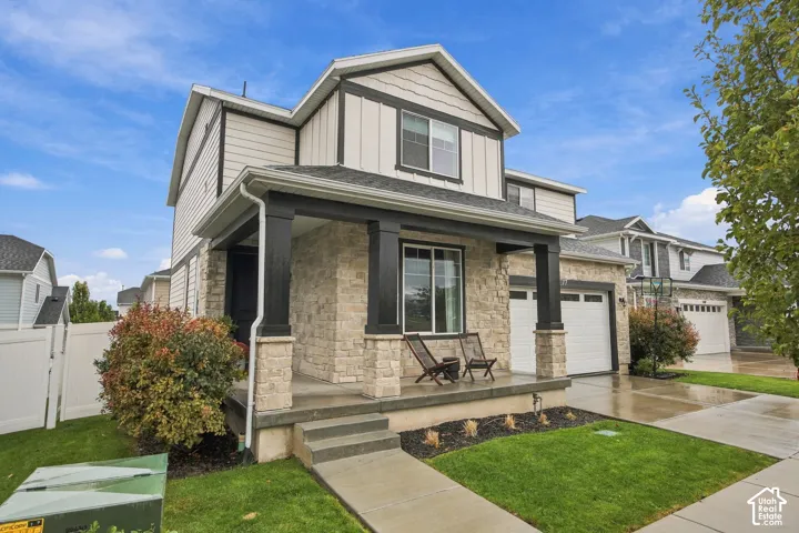 Two-story residence featuring stone veneer facade, board-and-batten siding, covered front porch with heavy timber columns, and concrete driveway