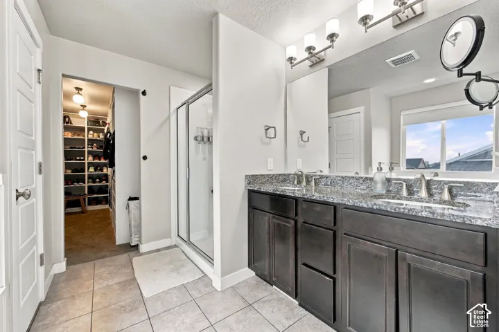 Double vanity with stone-finish countertop, dark wood-finish cabinetry, glass-enclosed shower, and built-in walk-in closet shelving