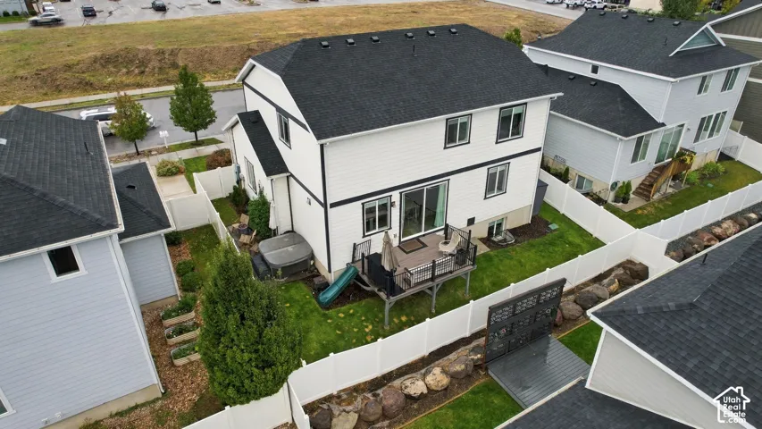 Exterior featuring white vinyl siding, a black asphalt shingle roof, elevated rear deck, white vinyl privacy fencing, and a terraced rock garden