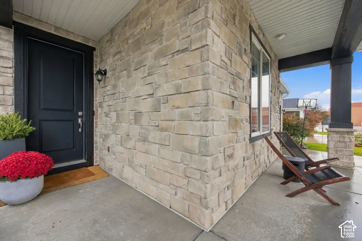 Covered entryway featuring natural stone veneer, dark-toned door casing, concrete porch flooring, and a stone-based support column