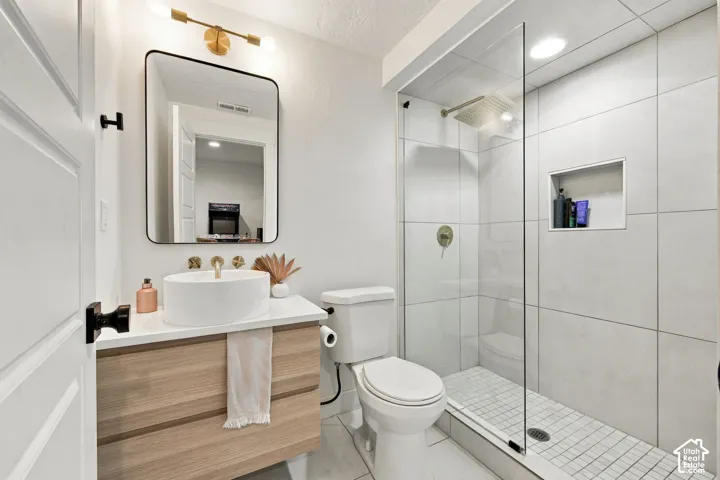Floating wood-finish vanity with a white vessel sink, gold-tone hardware, rectangular mirror, walk-in shower with large-format tile surround, and built-in wall niche