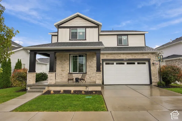 Two-story exterior featuring a stone facade, fiber cement board siding, covered front porch with stone-wrapped columns, and a double-car garage