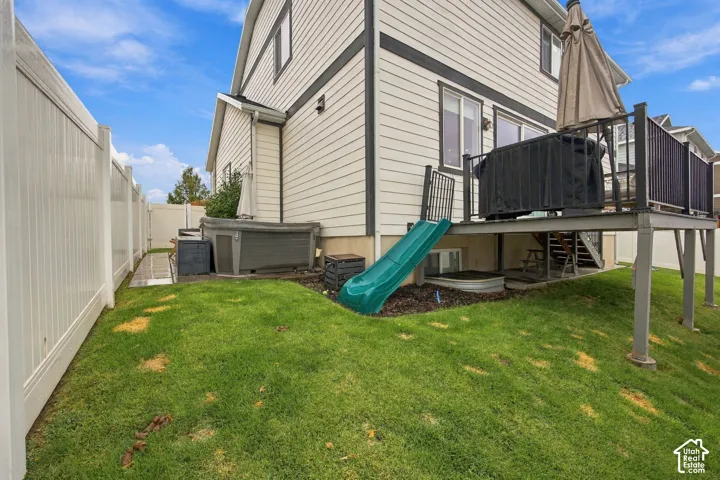 Exterior featuring horizontal lap siding, elevated deck with black metal railing, vinyl privacy fencing, and built-in hot tub