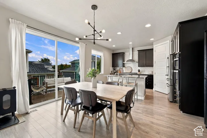 Open-concept kitchen featuring dark cabinetry, subway tile backsplash, stainless steel appliances, an island with stone countertop, and wood-finish flooring