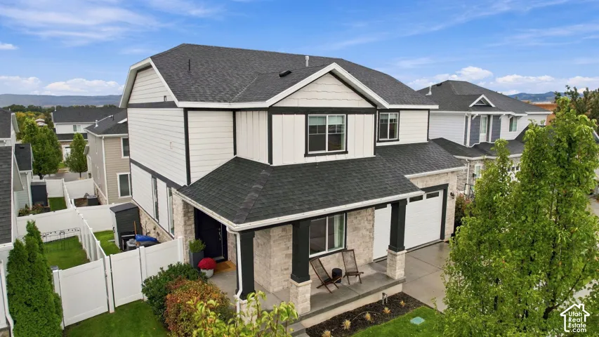 Two-story exterior featuring a mix of horizontal siding and board-and-batten siding, stone veneer accents, an asphalt shingle roof, and a covered front porch with timber-style pillars