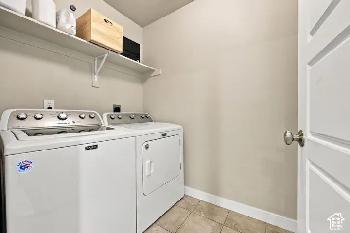 Laundry area featuring tile flooring, a wall-mounted storage shelf with metal brackets, and a multi-panel door with a brushed nickel knob