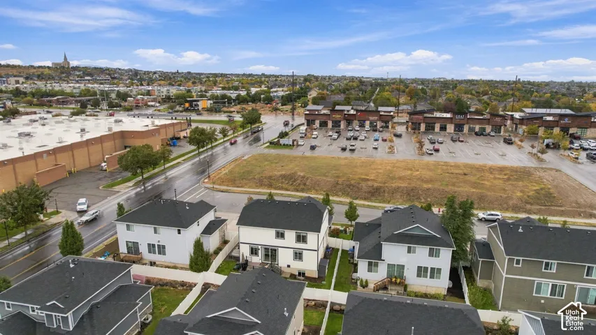 Aerial perspective featuring a residential subdivision with white-siding and dark-shingle roofline architecture, paved roadways, and proximity to commercial development