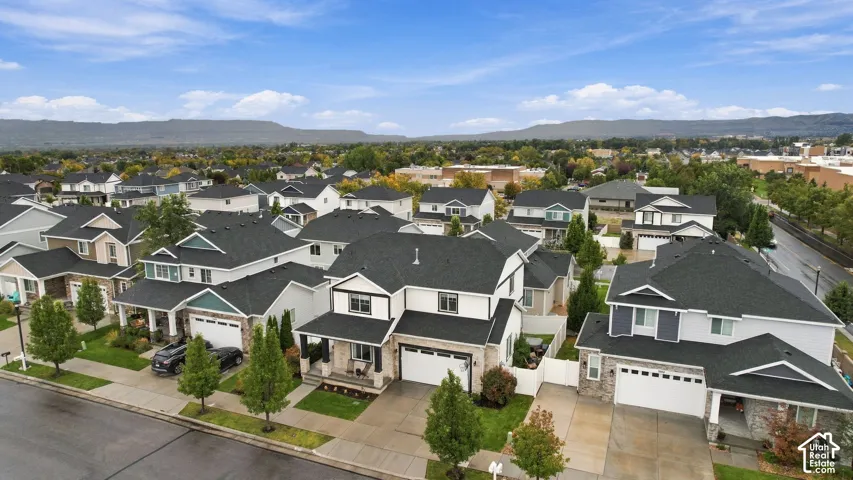 Aerial perspective of a multi-story residential exterior featuring a composite shingle roof, stone and siding facade, attached two-car garage, concrete driveway, and mountain backdrop