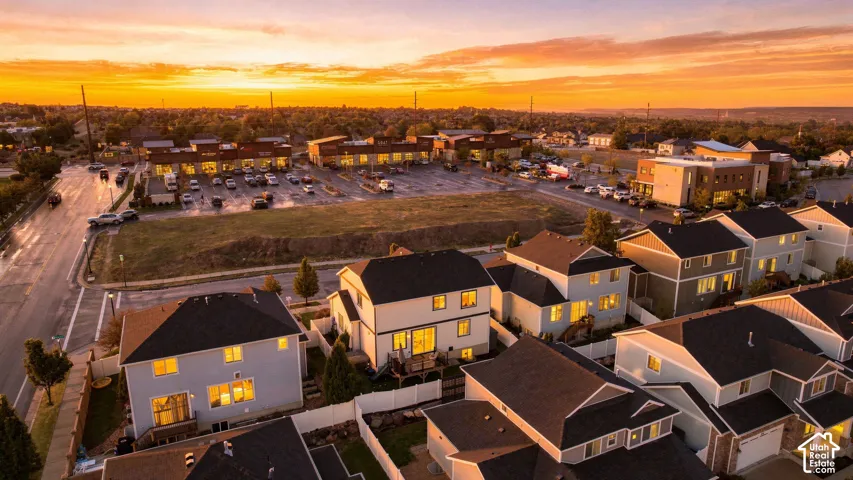 Aerial perspective of a residential neighborhood featuring multi-story dwellings, fenced backyards, paved street infrastructure, and proximity to a commercial retail center