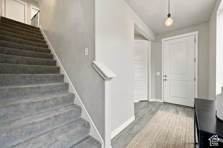 Foyer featuring wood-finish flooring, a neutral color palette, carpeted staircase with a partial wall railing, and a multi-panel entry door with hardware