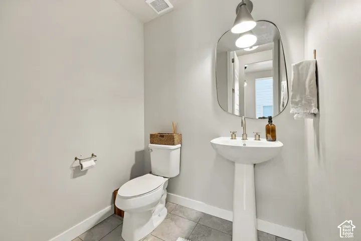 Powder room featuring a white pedestal sink with metallic widespread faucet, large-format tile flooring, a uniquely shaped wall-mounted mirror, and decorative wall-mounted lighting