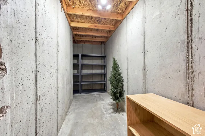 Storage area featuring exposed concrete walls, exposed wood-joist ceiling, and concrete flooring
