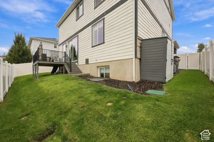 Exterior of the property featuring light-colored horizontal siding, an elevated deck with metal railing, a grass lawn, and white vinyl privacy fencing