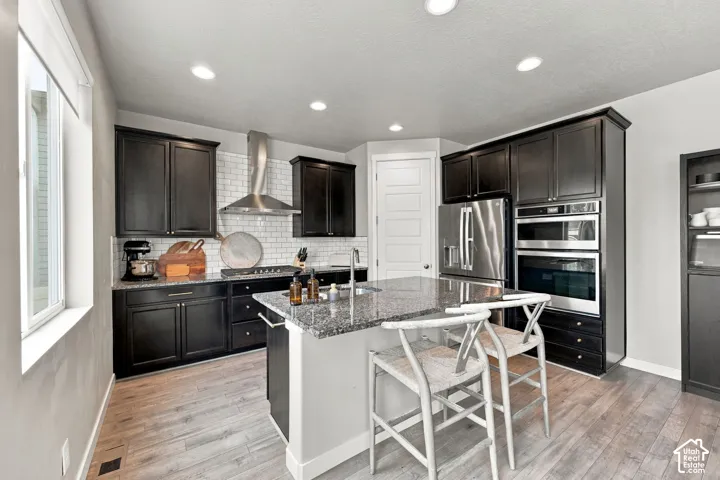 Kitchen featuring dark cabinetry, stone countertops, subway tile backsplash, stainless steel appliances, and a center island