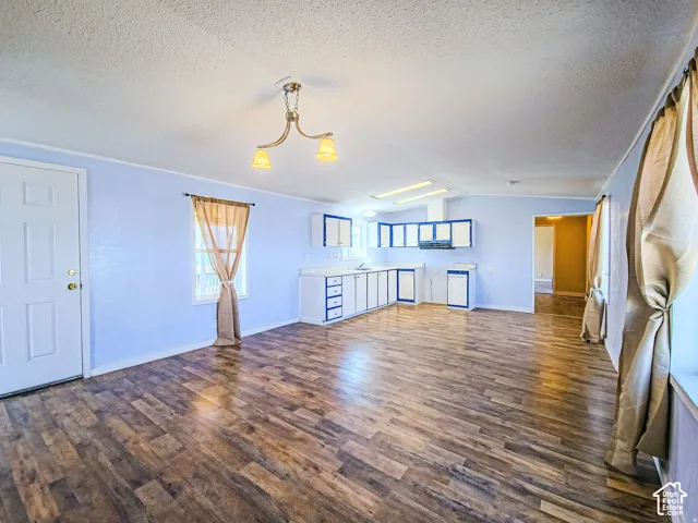 Open-concept interior featuring wood-finish flooring, cabinetry with contrasting trim, recessed ceiling lighting, and a multi-arm chandelier