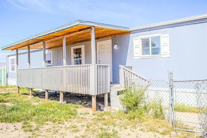 Covered wooden front porch with horizontal railing, paneled siding, shuttered windows, and chain-link perimeter fencing