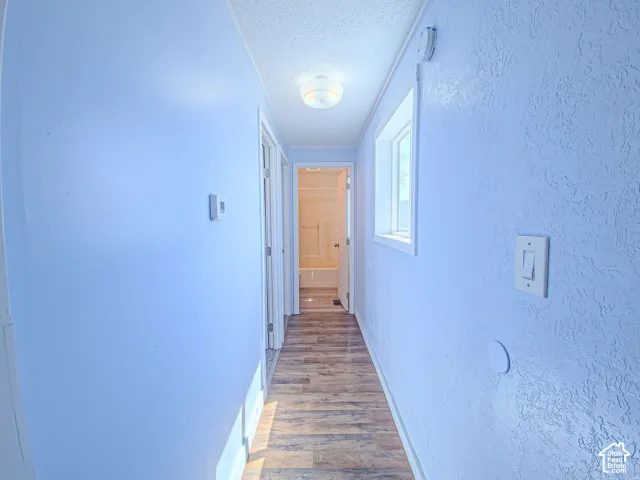 Hallway featuring wood-finish flooring, textured wall surfaces, a flush-mount ceiling light fixture, and a window