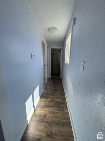 Hallway featuring wood-finish flooring, textured walls, and a ceiling-mounted light fixture