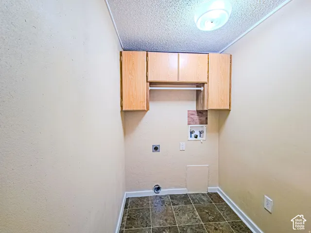 Utility space featuring stone-finish tile flooring, wood-veneer cabinetry with an integrated hanging rod, and dedicated appliance hookups