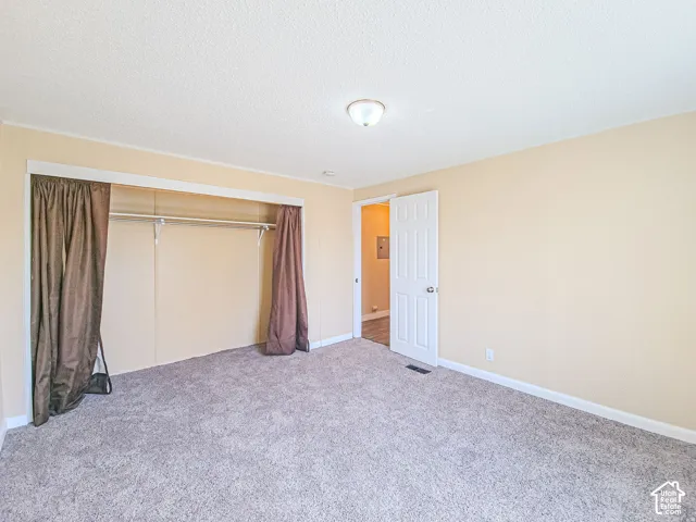 Neutral wall finish, gray carpeting, six-panel interior door, and built-in closet with overhead shelf and rod