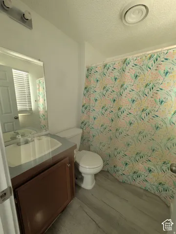Bathroom featuring wood-finish cabinetry, a rectangular sink with integrated countertop, wall-mounted mirror, and wood-finish flooring