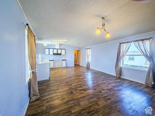 Open-concept interior featuring wood-finish flooring, multi-light hanging fixtures, and cabinetry with integrated range hood