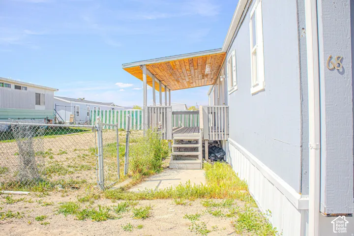 Exterior elevation featuring a covered wooden deck, light blue siding, and a chain-link fenced perimeter