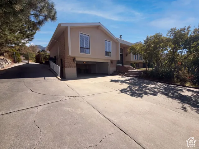 Split-level exterior featuring brick and stucco siding, a built-in garage, a concrete driveway, and stone-finished entryway stairs