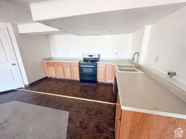 Kitchen featuring wood-finish cabinetry, solid-surface countertops, dual-basin sink with a gooseneck faucet, black freestanding electric range, and tile flooring