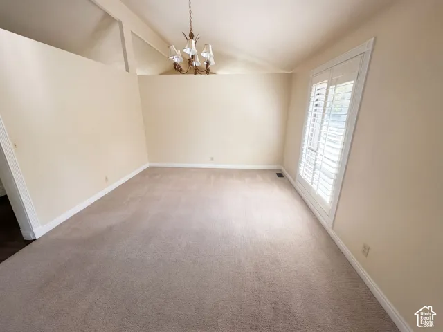 Vaulted ceilings, neutral carpeting, multi-light chandelier, and plantation shutters