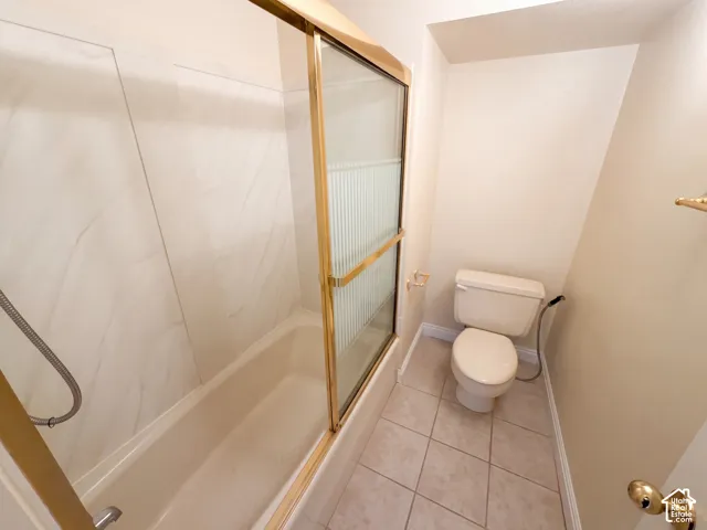 Bathtub and shower combination featuring large-format surround tile, gold-finished sliding glass enclosure, hand-held shower fixture, and ceramic tile flooring