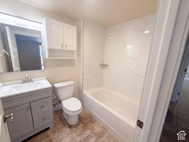 Bathroom featuring a grey vanity with a white countertop, wall-mounted white cabinetry, a tub-shower combination with light-toned tiled surround, and multi-toned tile flooring